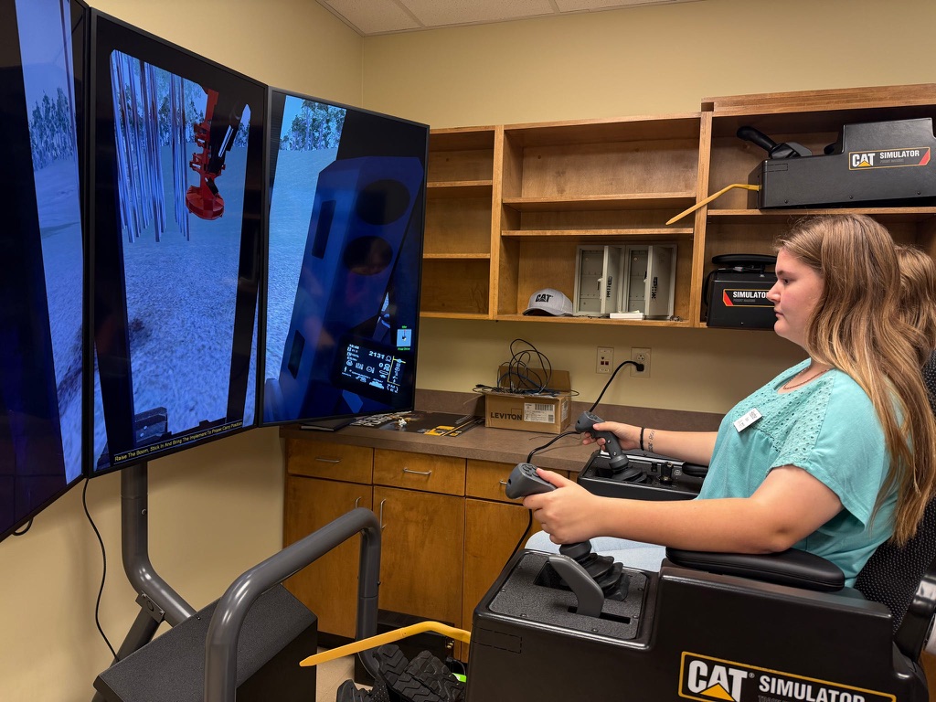 Teen girl moves hand-held controllers on a skidder simulator. 