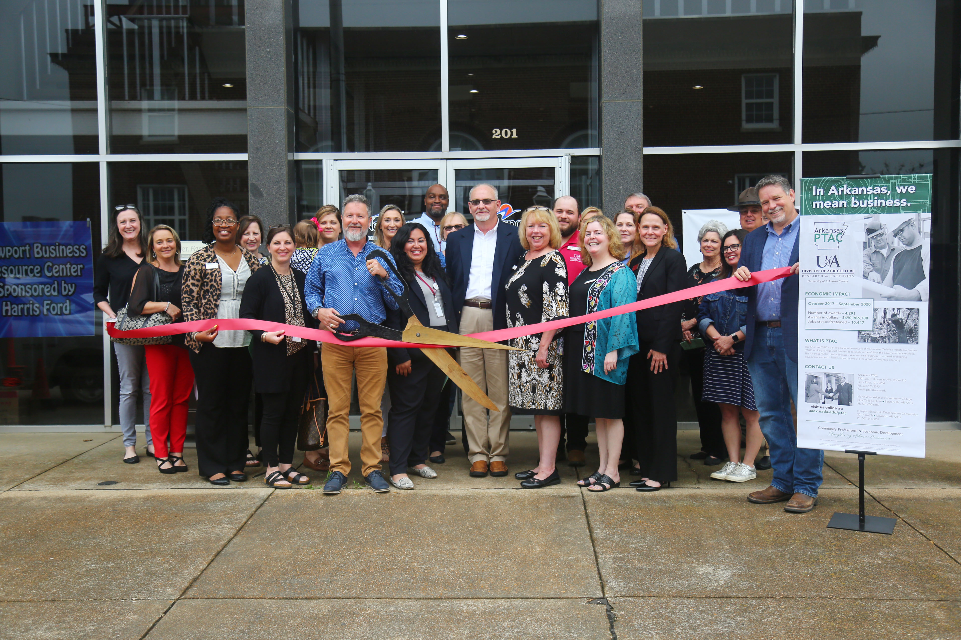 A group of people smile in front of the new Newport office during the ribbon cutting ceremony.