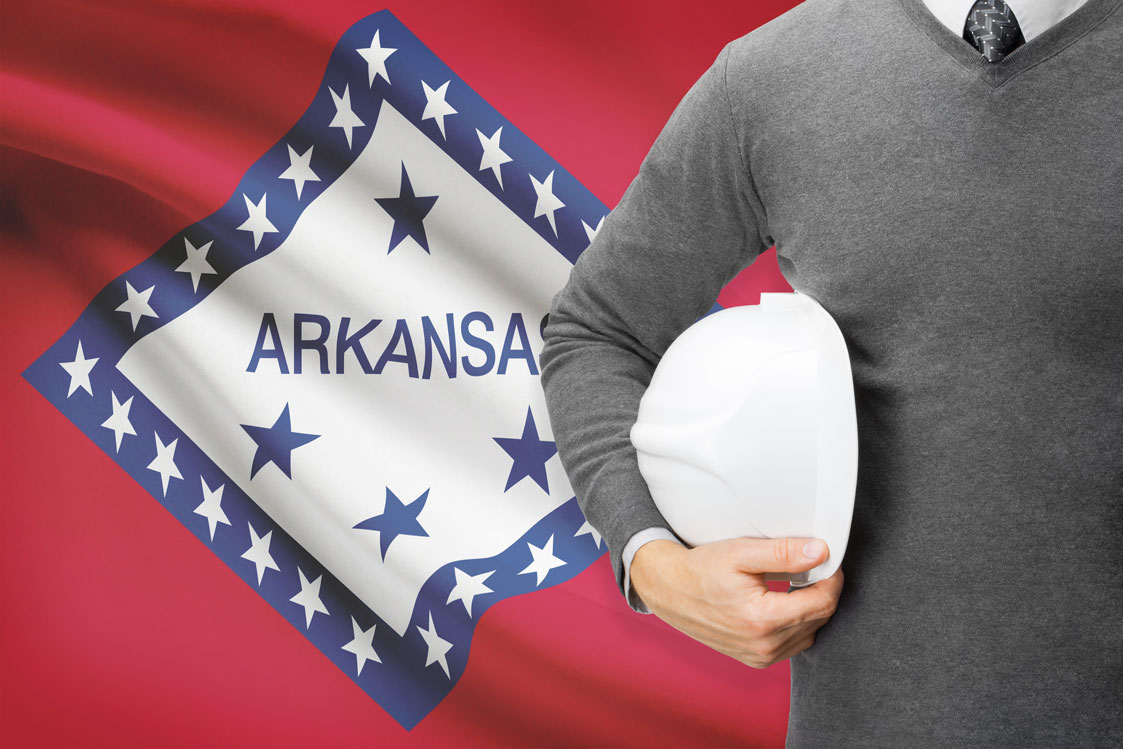 Man standing in front of Arkansas flag holding a hard hat
